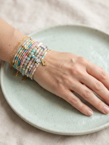 Macro close-up of hands wearing stacked bead bracelets, resting on a pastel ceramic plate, natural daylight.