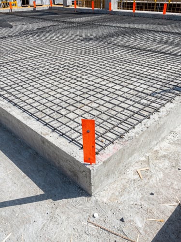 Wide-angle shot of a freshly poured concrete foundation with steel rebar grids, bright daylight, high-contrast safety orange markers, sharp focus