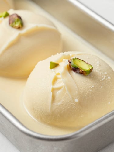 Bright editorial food photography of freshly folded pistachio gelato being sculpted into a metal pan, soft natural daylight, creamy pastel tones, close-up macro lens, shallow depth of field.