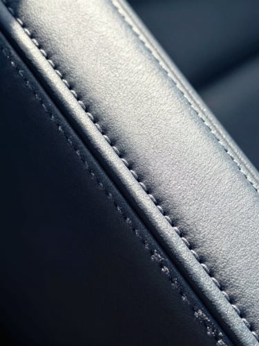 Extreme close-up of pristine automotive leather stitching, high-key natural light, deep navy and silver tones, sharp focus, 35mm