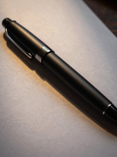 Close-up of a premium matte black fountain pen resting on heavy textured paper, sharp side lighting, golden-hour reflection, professional executive desk environment