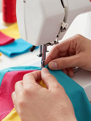 Hands carefully stitching a colorful pet garment on a sewing machine, soft natural workshop light, detailed close-up of fabric textures