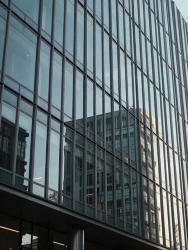 Wide environmental view of a modern glass-and-steel corporate headquarters facade, sharp architectural shadows, cool natural daylight, minimal composition.