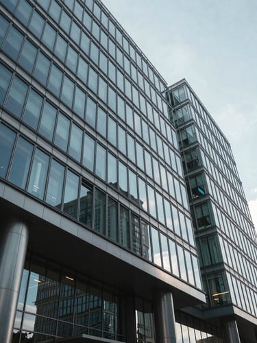 Wide environmental shot of a modern glass-and-steel corporate headquarters in cool natural daylight, architectural shadows, sharp angles, clean reflection.