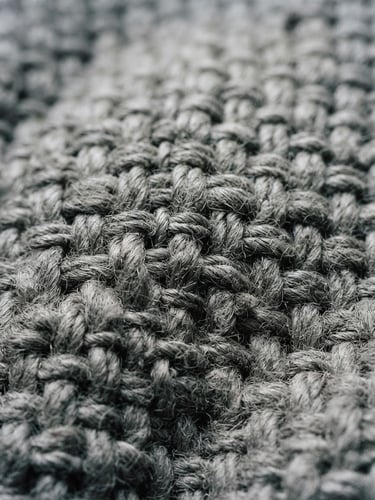 Macro detail shot of heavy-gauge desaturated grey cotton fabric weave under high-contrast studio lighting, sharp dark shadows, 35mm