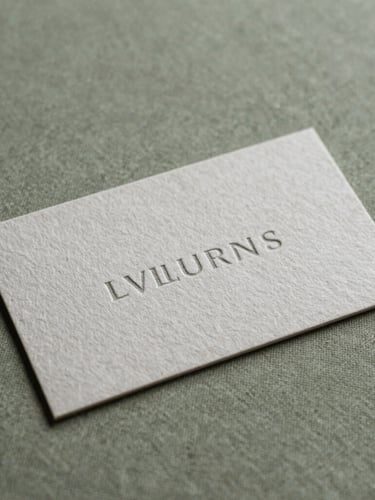 A close-up of beautifully embossed heavy cotton paper business cards with minimalist typography, resting on a soft olive green linen surface.