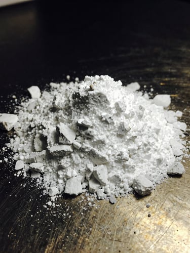Macro photograph of pure white crystalline potassium feldspar powder on a dark metallic laboratory surface, razor-sharp focus, low-key gold lighting, 35mm