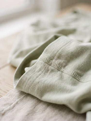 Softly folded organic cotton loungewear, close-up of delicate seams, diffused morning light, shallow depth of field, off-center composition to the right.