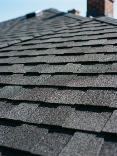 Close-up of new architectural shingles on a completed roof, crisp lines, natural daylight, deep charcoal tones, sharp focus, 35mm