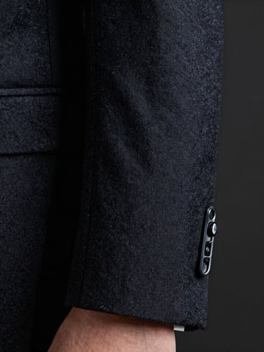 Macro detail of a tailored dark wool suit sleeve and a subtle, low-profile earpiece, cool high-contrast lighting, dark background.
