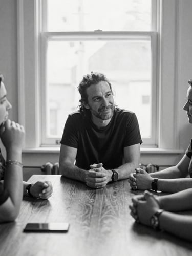 High-contrast black-and-white environmental portrait of community organizers in active discussion around a wooden table, soft natural window light, candid 35mm film style