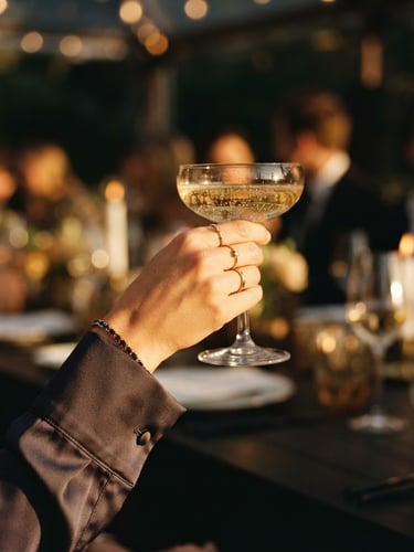 Close-up of a hand in a silk cuff holding a champagne glass, warm golden hour light, cinematic editorial style, 35mm film