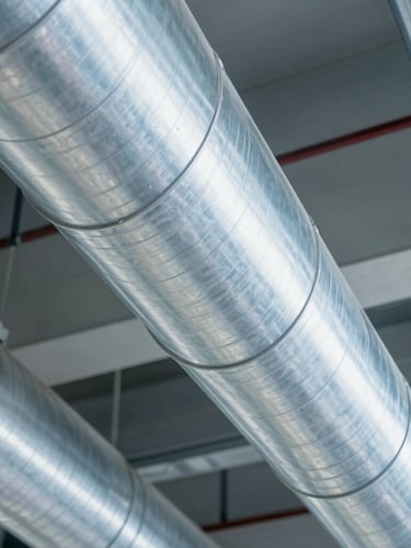 Sharp commercial photography of an immaculate metallic duct interior, bright cool-toned technical lighting, clean steel surfaces showing zero dust, 35mm lens.