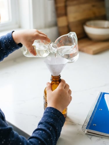 Close-up of a child's hands carefully pouring vinegar into a glass bottle using a small paper funnel, bright natural daylight, clean white kitchen counter background, energetic blue accent on a notebook nearby, sharp focus, 35mm