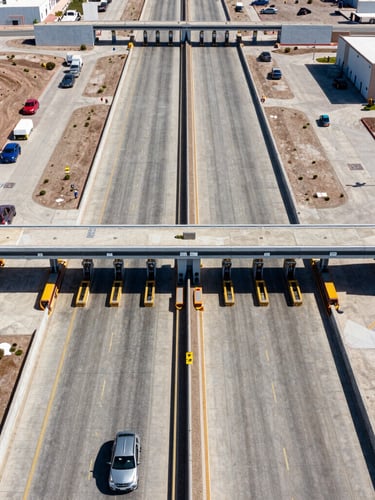 Symmetrical high-altitude aerial view of a structured border customs port of entry in Mexicali, sharp daylight, clean concrete lanes, geometric architecture.