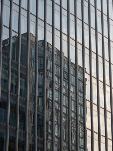 Tight macro architectural detail of a modern high-rise glass facade with sharp morning shadows, high-contrast structural lines, 35mm architectural lens.