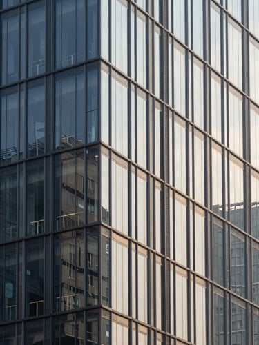 Architectural crop of a modern high-rise glass facade, sharp morning daylight, high-contrast shadows, 35mm architectural lens