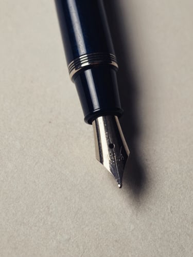 Macro close-up of a classic fountain pen resting on heavy textured ivory paper, dramatic side-lighting, deep navy shadows, high-contrast editorial style.