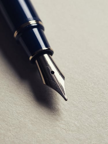 Macro close-up of a classic fountain pen nib resting on heavy, textured ivory paper, dramatic side-lighting, deep navy shadows, high contrast