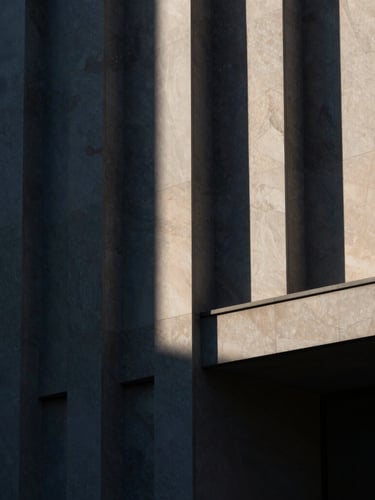 High-contrast architectural detail of a modern library facade, geometric stone patterns, dramatic side-lighting, deep navy and warm ivory tones, moody editorial style