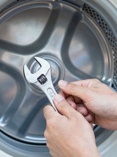A close-up shot of clean hands using a wrench on a metallic dryer drum, bright natural daylight, 50mm, focus on mechanical details.