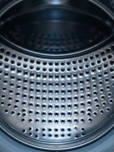 Straight-on macro shot of a clean stainless steel washing machine drum interior, bright workshop lighting, sharp focus on metallic texture, 50mm