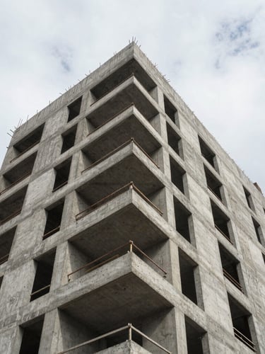 Low-angle heroic shot of a raw concrete mid-rise building under construction, stark geometric shadows, overcast daylight emphasizing texture