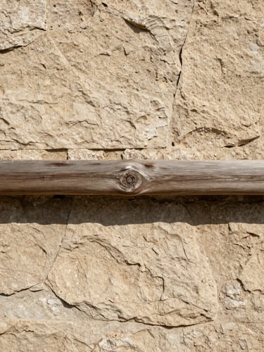 Gros plan sur un mur en pierre calcaire beige et une poutre en bois brut brossé, texture organique et lumière rasante chaleureuse