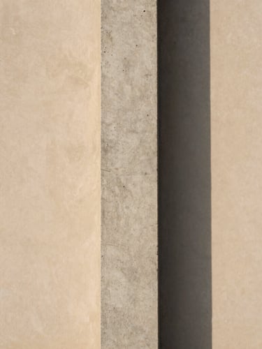A raw concrete column casting a soft, long shadow on a warm-toned plaster wall, minimalist architectural photography, diffused natural daylight