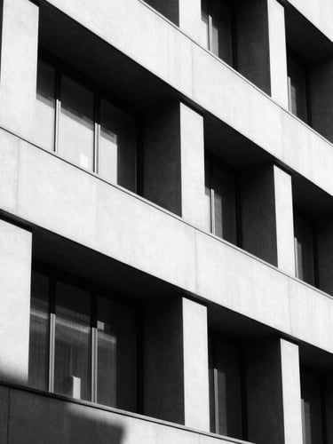 High-contrast black and white architectural detail of a modern corporate building facade in Milan, sharp geometric shadows, minimalist aesthetic, 35mm lens.
