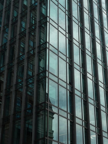 Low-key architectural photograph of a modern glass high-rise facade reflecting cool neon-mint light patterns, sharp geometric shadows, high-contrast composition