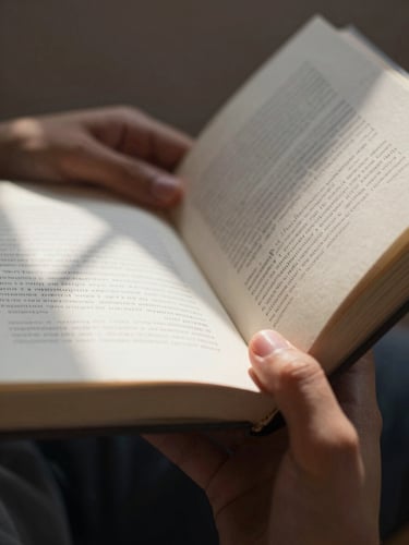 Tight macro shot of a student's hands holding an open book under natural daylight, deep shadows framing the textured paper pages, focused atmosphere.