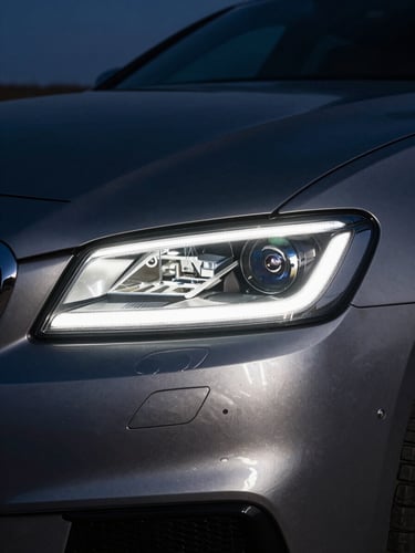 Macro close-up of a luxury sedan headlight cutting through West Texas twilight, sharp metallic silver reflections on charcoal paint, high-contrast night shot, 35mm
