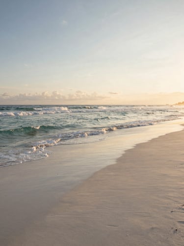 Wide panoramic shot of a secluded white sand beach in Bali during golden hour, gentle waves kissing the shore, soft warm sunlight, no crowds.