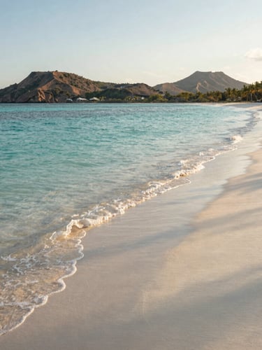 Wide environmental shot of a secluded white sand beach in Lombok, crystal clear turquoise water gently lapping the shore, volcanic hills in the far distance, warm golden hour light