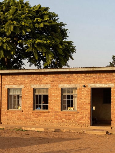 Warm editorial photography of a simple, clean brick orphanage building in Manica under golden hour light, lush green trees around