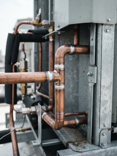 A close-up of pristine copper piping welds on a commercial condenser unit, bright utility lighting, cool metallic tones, sharp focus.