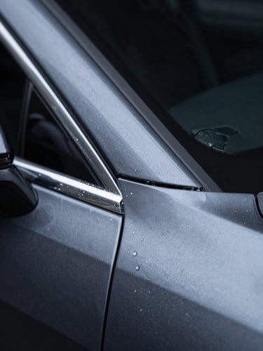 Extreme close-up macro shot of a vehicle paint protection film edge transition on a dark charcoal car panel, cool studio side lighting revealing the film's invisible boundary against the original paint, dark background, 2-3cm framing showing material clarity and zero air bubble installation