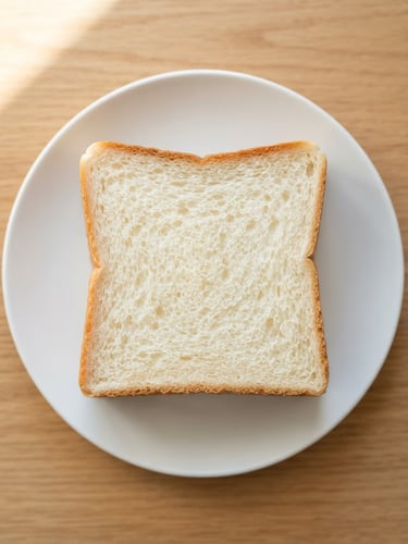 Dead-on geometric overhead shot of a perfectly square shokupan slice on a minimalist white plate, bright morning window light highlighting the uniform crumb structure, warm golden crust edges.