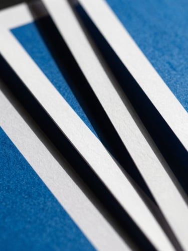 Extreme close-up of high-contrast physical brand collateral, sharp paper edges, direct hard sunlight, deep charcoal shadows, cool blue ink.