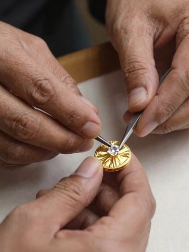 A master artisan's hands meticulously placing an uncut Polki diamond into a pure gold foil setting using traditional hand tools, warm studio lighting