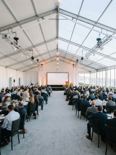 Wide shot of a large, pristine white structural tent interior set up for a corporate event, with elegant lighting and a stage visible, under crisp coastal daylight, professional and clean composition.