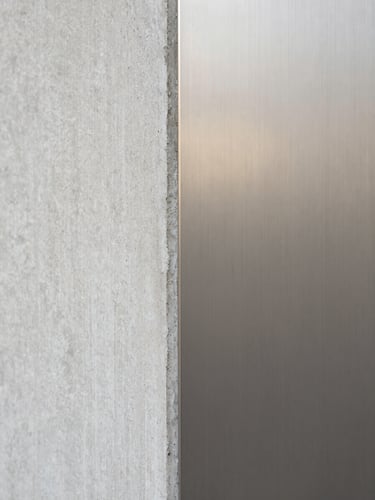 Extreme close-up of raw textured concrete meeting smooth brushed steel, soft diffused side daylight, neutral muted tones, architectural detail study