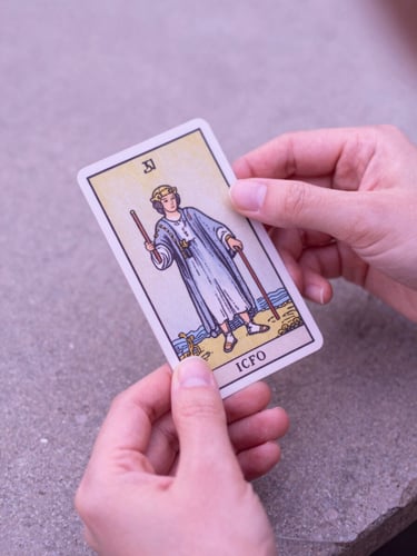 Soft-focus hands with clean manicures holding a single tarot card over a stone surface, luminous morning light, dusty pink tones, 35mm
