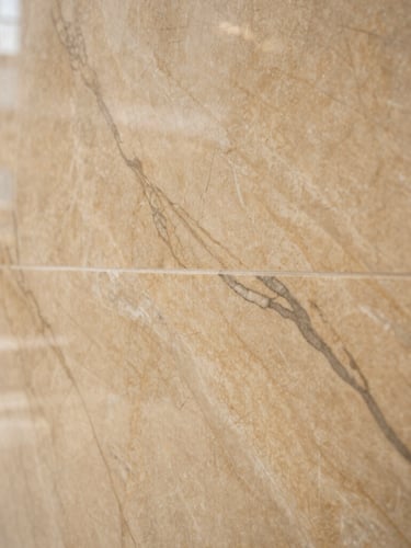Detailed close-up of premium bookmatched marble veins on a wall, warm sand tones, architectural interior detail, soft natural light, sharp focus