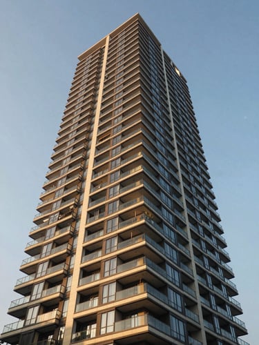 Low-angle architectural photography of a modern Mumbai residential high-rise with glass balconies reflecting golden-hour sunlight against a clear sky