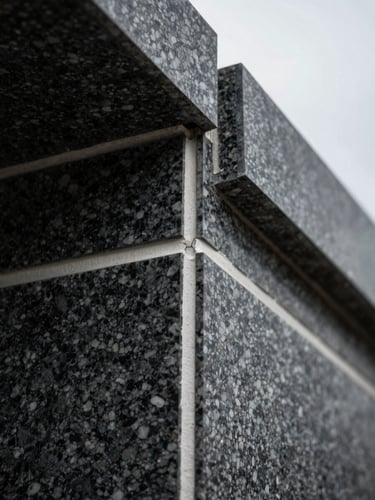 Extreme close-up of precision masonry joint on completed building facade, dark granite meeting white mortar channel, overcast diffuse light, architectural material detail, no people