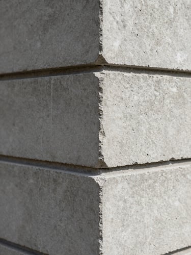 Extreme close-up of a wall junction where raw concrete meets a precision-cut stone cladding panel — sharp right-angle intersection, hairline mortar joint, matte surface textures under diffuse north-facing daylight, no people, no furnishings, emphasis on material tolerance and craft detail