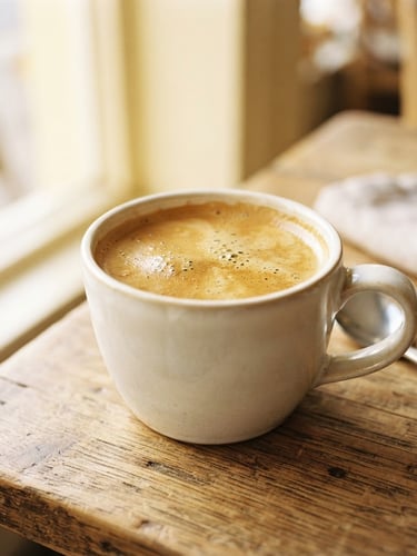 Sun-drenched portrait of a freshly poured coffee with rich crema on a wooden table, soft morning daylight, cream and soft yellow tones, shallow depth of field, 35mm.