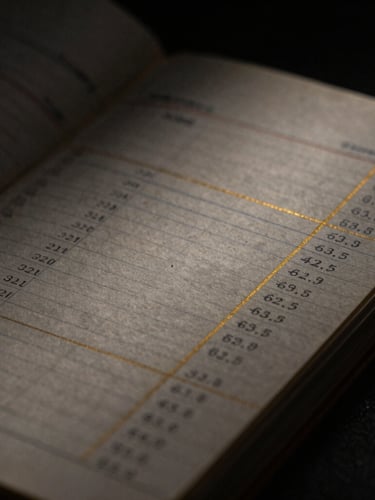 Dark editorial macro photography of a vintage financial ledger with handwritten numbers, low-key dramatic side-lighting, golden ink accents, deep charcoal background, 35mm
